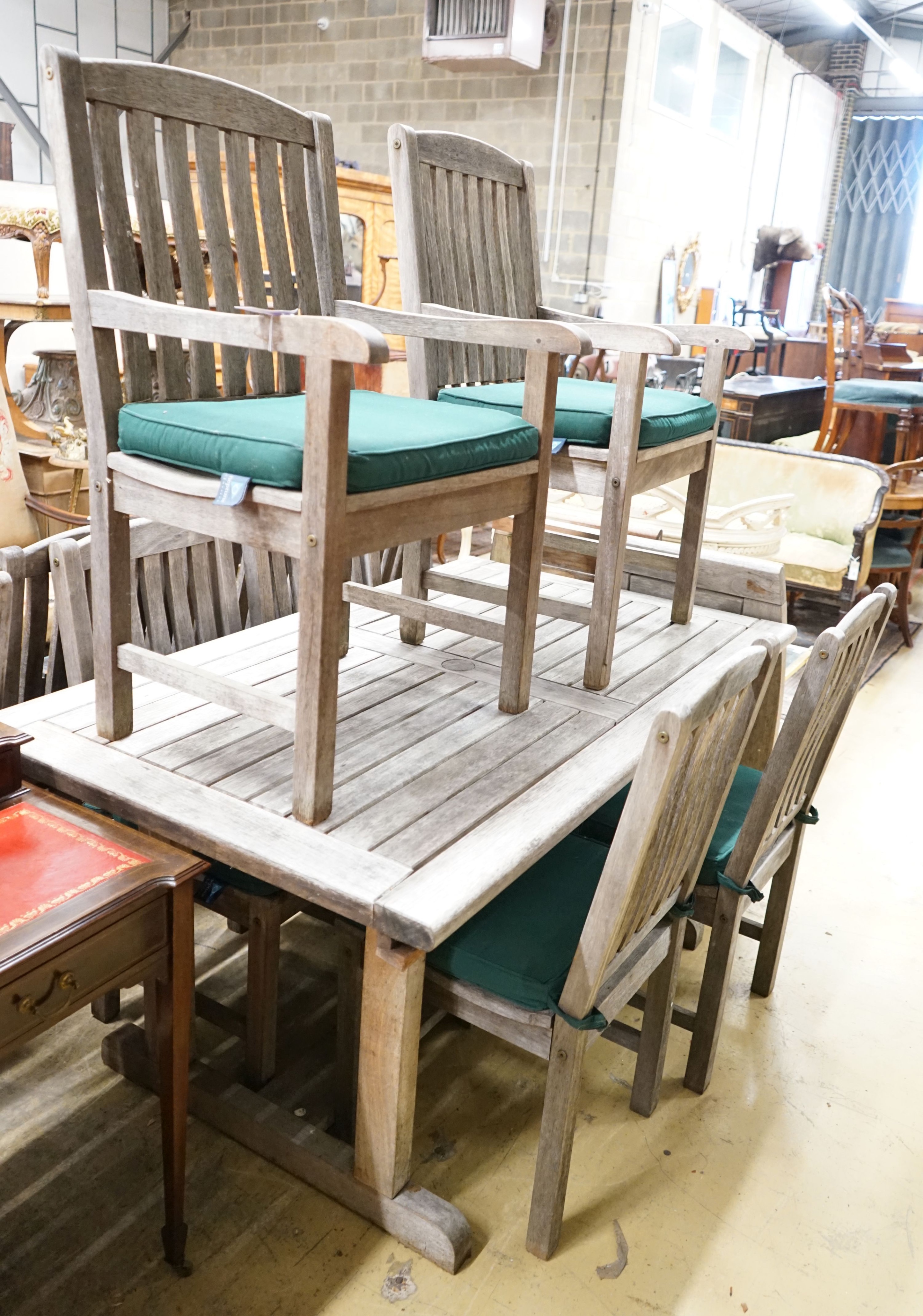 A rectangular weathered teak garden table with removable end sections, together with ten garden chairs, with seat pads, two with arms